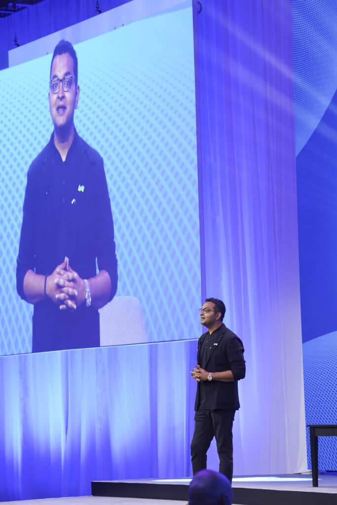 Executive speaker delivers a corporate presentation on stage with dynamic LED screen backdrop, captured by Christie’s Photographic Solutions.