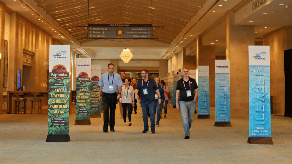 Attendees walk through a pre-function hallway featuring branded signage and corporate activations, captured by Christie’s Photographic Solutions