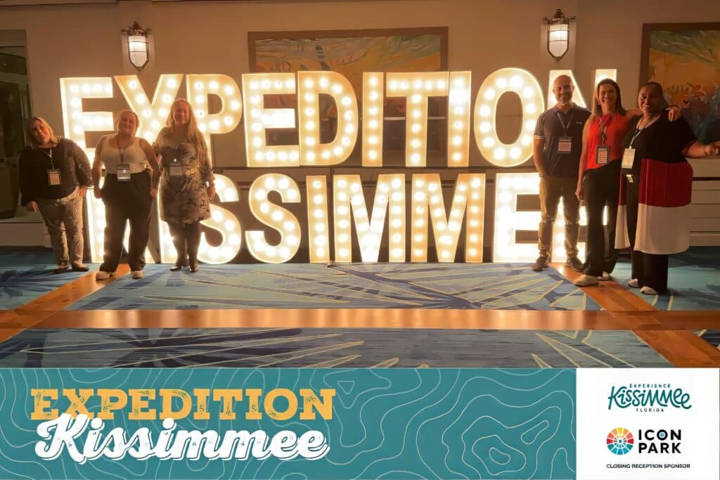 Group photo in front of illuminated marquee sign at an event, captured by Christie’s Photographic Solutions.