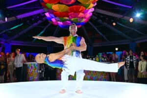 Vibrant live performance with acrobatic dancers in rainbow attire during a corporate evening celebration, captured by Christie’s Photographic Solutions.