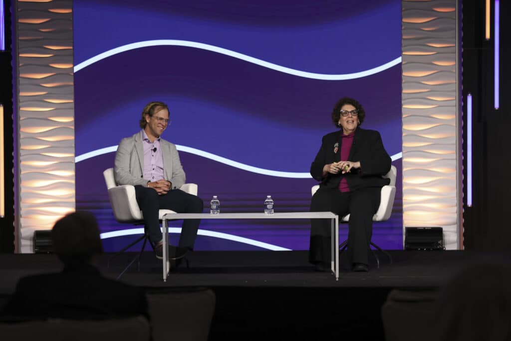 Two speakers seated on stage during a conference session at, captured by Christie’s Photographic Solutions.