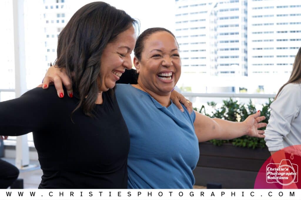 Corporate wellness event attendees sharing a joyful candid moment during a corporate gathering, captured by Christie’s Photographic Solutions.