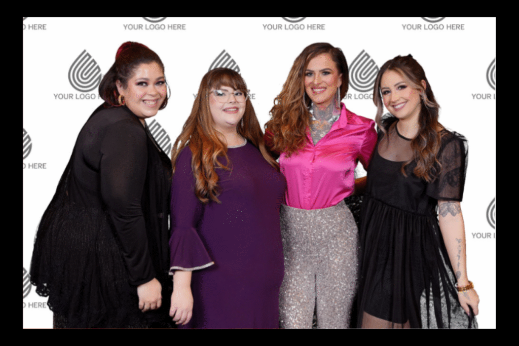 Four event guests posing together at a branded step-and-repeat photo station, captured by Christie’s Photographic Solutions.
