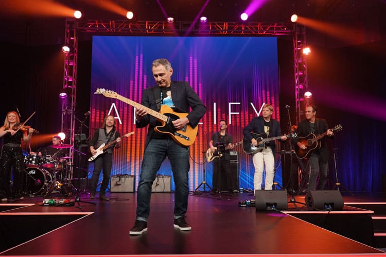 Live band performance energizing the crowd on a vibrant stage at a corporate event, captured by Christie’s Photographic Solutions.