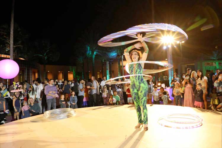 Professional hula hoop artist performing at a lively corporate event with an engaged evening crowd, captured by Christie’s Photographic Solutions.