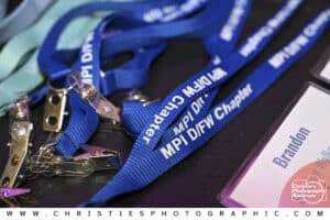 Branded MPI DFW Chapter lanyards and attendee name badge displayed on a registration table, captured by Christie’s Photographic Solutions.