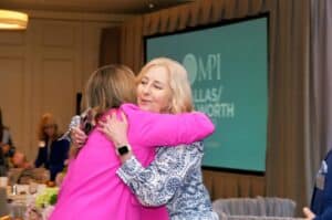 Two attendees sharing a warm embrace during a corporate networking event, captured by Christie’s Photographic Solutions.