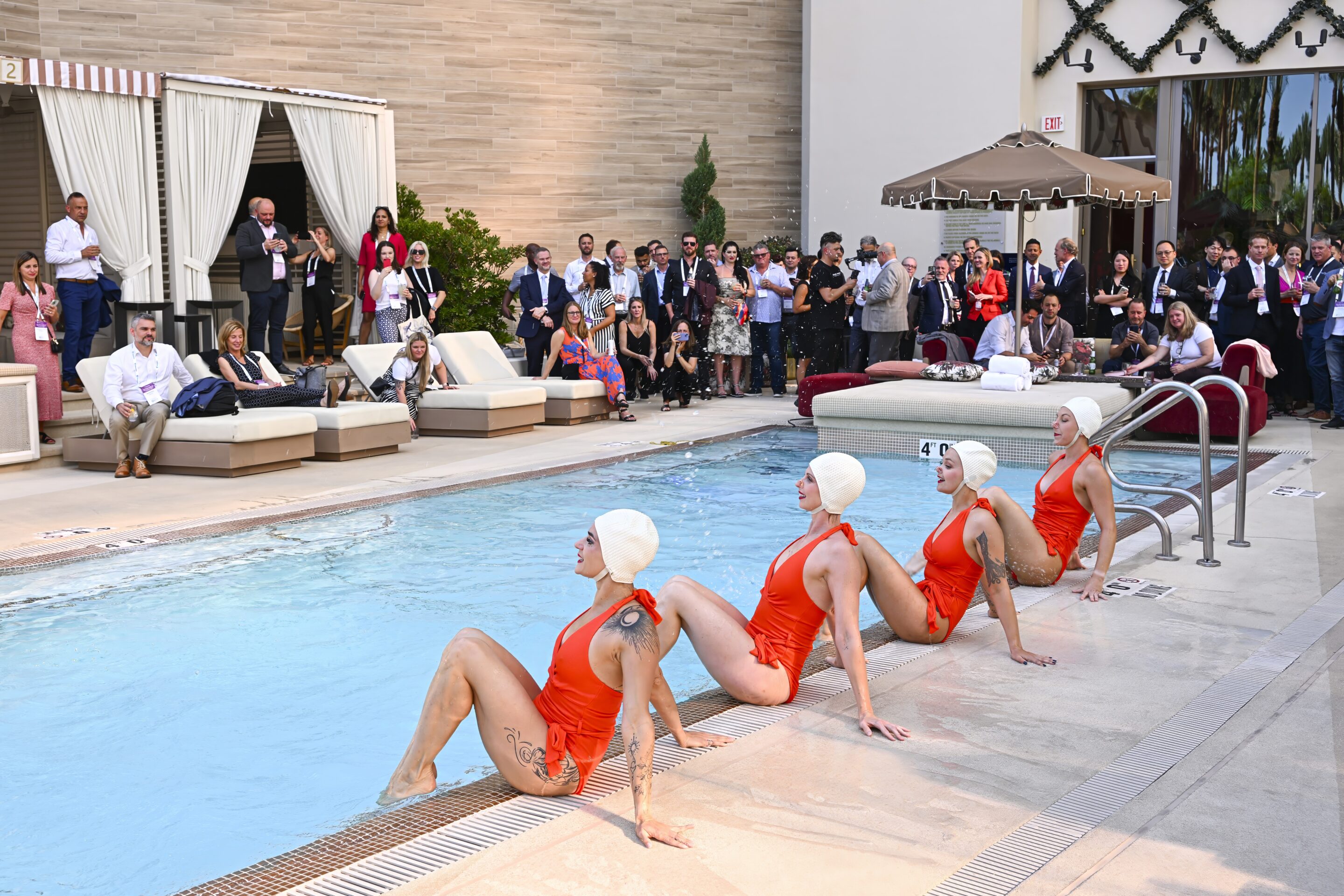 Synchronized performers in vintage swimwear entertaining guests beside a resort pool during a corporate reception, captured by Christie’s Photographic Solutions