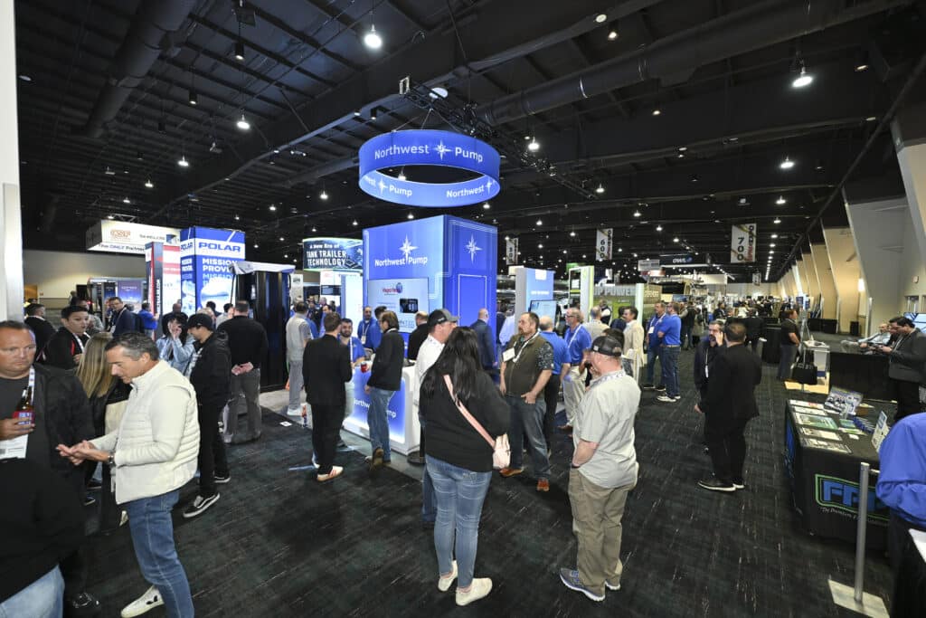 Attendees networking and exploring branded booths within a busy trade show exhibit hall, captured by Christie’s Photographic Solutions.