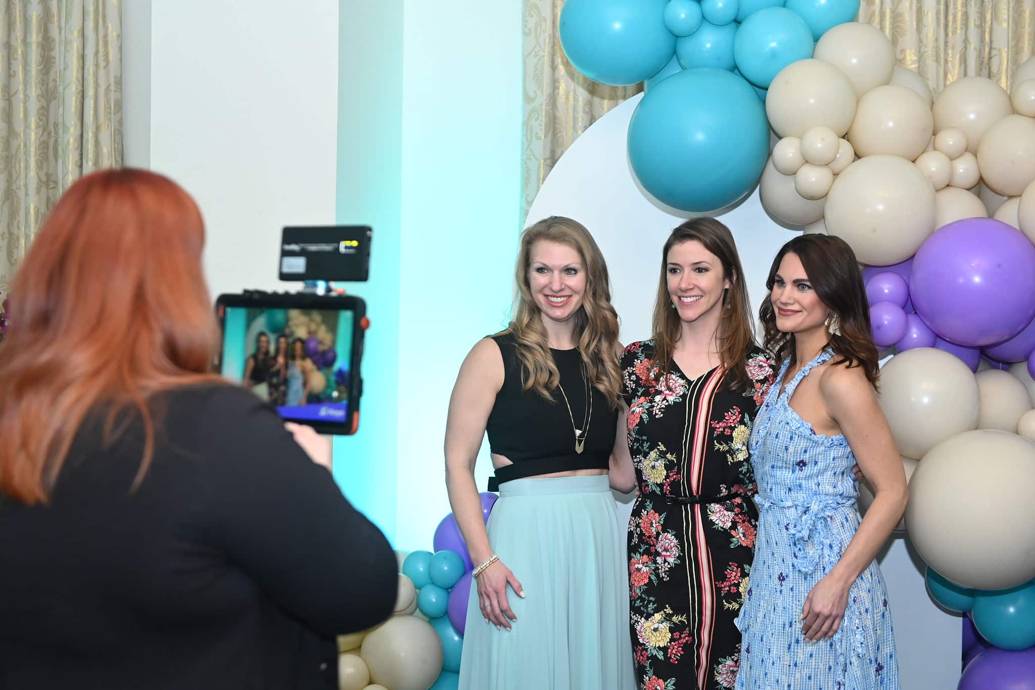 Guests posing in front of a custom balloon backdrop while using the iLite Roaming Photo Booth, captured by Christie’s Photographic Solutions.